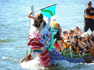 flag catcher leaning forward over nose of surging ceremonial dragon boat to catch the finish flag